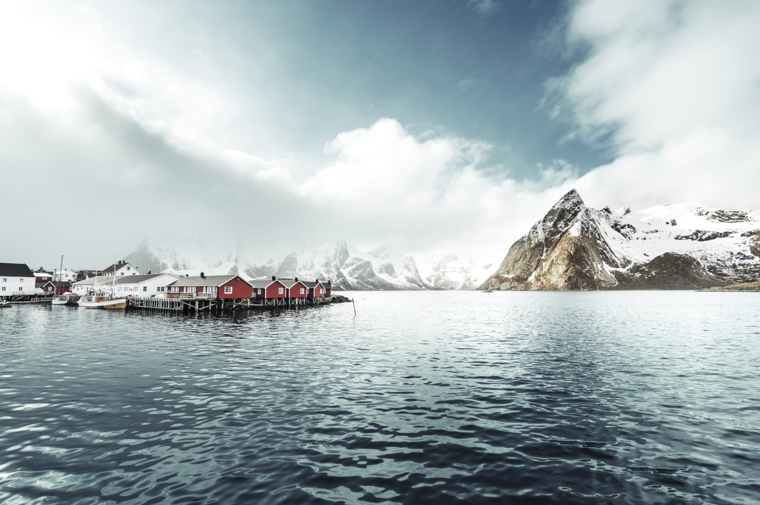 Norwegische Fjordlandschaft mit roten Fischerhäusern, schneebedeckten Bergen und ruhigem Wasser